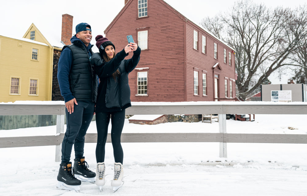 a man and a woman taking a selfie on an outdoor snowy ice rink in Bauer ice skates